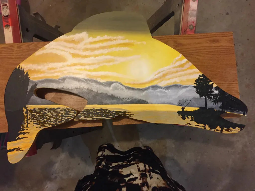 Fish Wood Cutout Art: Acrylic painted scene inside a fish silhouette featuring a fisherman casting a line against a lake and sunset landscape.