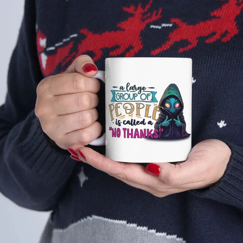 Person holding a white ceramic mug that says "A large group of people is called a NO THANKS" with a hooded cartoon character.